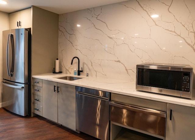 kitchen with appliances with stainless steel finishes, dark hardwood / wood-style floors, light stone countertops, white cabinets, and sink