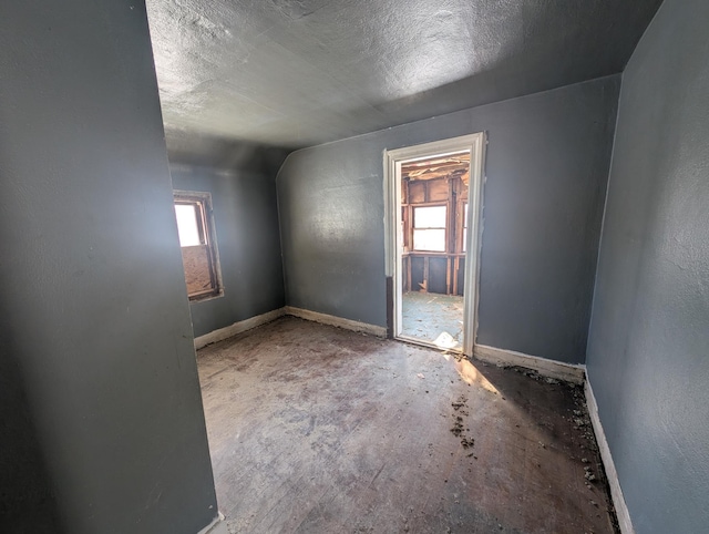 spare room featuring a textured ceiling, lofted ceiling, a wealth of natural light, and baseboards