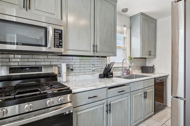 kitchen with stainless steel appliances, sink, gray cabinets, light tile patterned floors, and light stone countertops