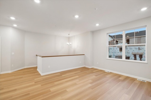 spare room featuring a notable chandelier and light wood-type flooring