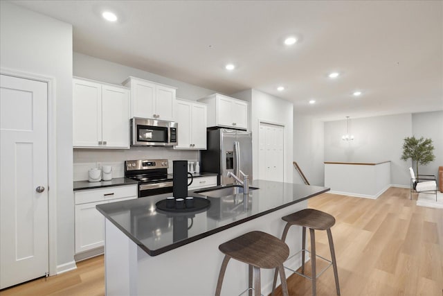 kitchen with an island with sink, a breakfast bar area, appliances with stainless steel finishes, white cabinetry, and sink