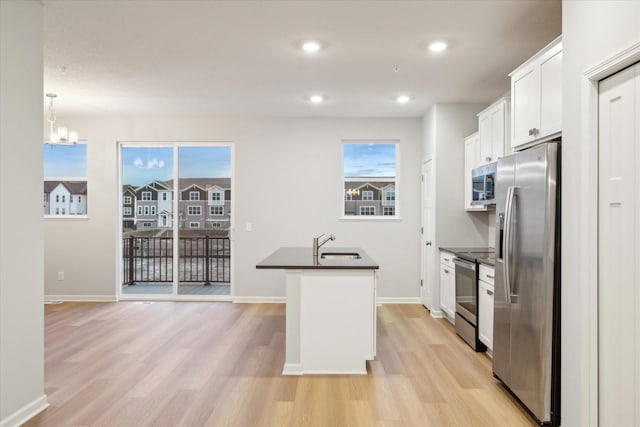 kitchen featuring appliances with stainless steel finishes, an island with sink, pendant lighting, white cabinets, and light hardwood / wood-style flooring