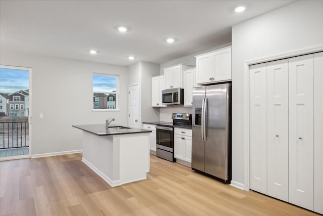 kitchen with stainless steel appliances, sink, white cabinets, light hardwood / wood-style floors, and a center island with sink