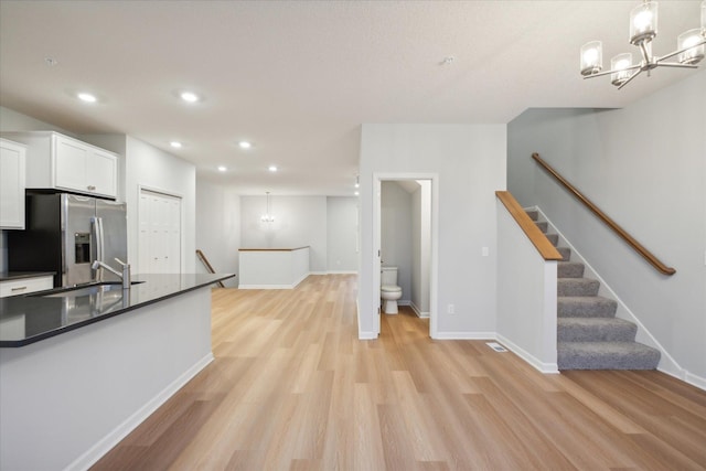 kitchen featuring light hardwood / wood-style floors, stainless steel fridge with ice dispenser, hanging light fixtures, sink, and white cabinetry