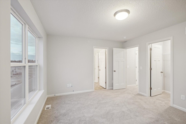 unfurnished bedroom with a textured ceiling, a walk in closet, light carpet, and ensuite bath