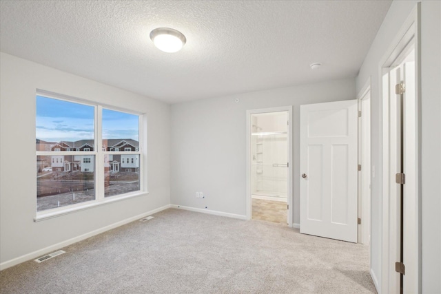 unfurnished bedroom with a textured ceiling, connected bathroom, and light colored carpet