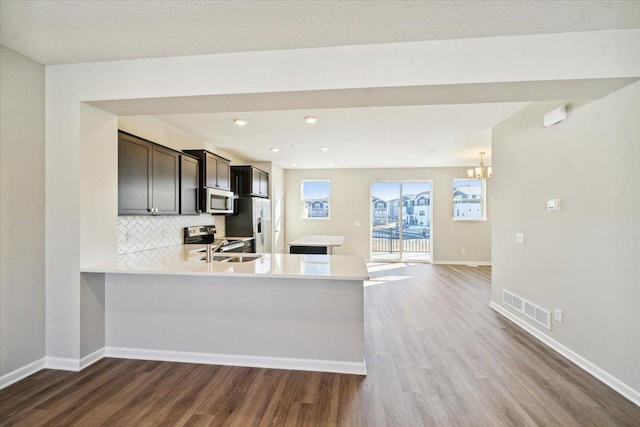 kitchen featuring stainless steel appliances, hardwood / wood-style flooring, kitchen peninsula, backsplash, and dark brown cabinetry