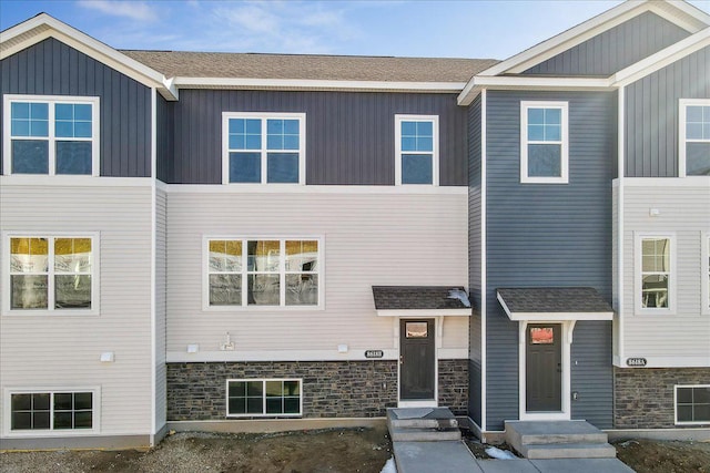 townhome / multi-family property featuring stone siding, a shingled roof, and board and batten siding