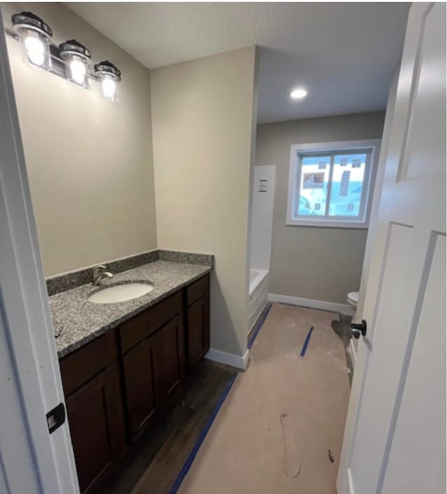 bathroom featuring wood-type flooring, a tub, vanity, and toilet