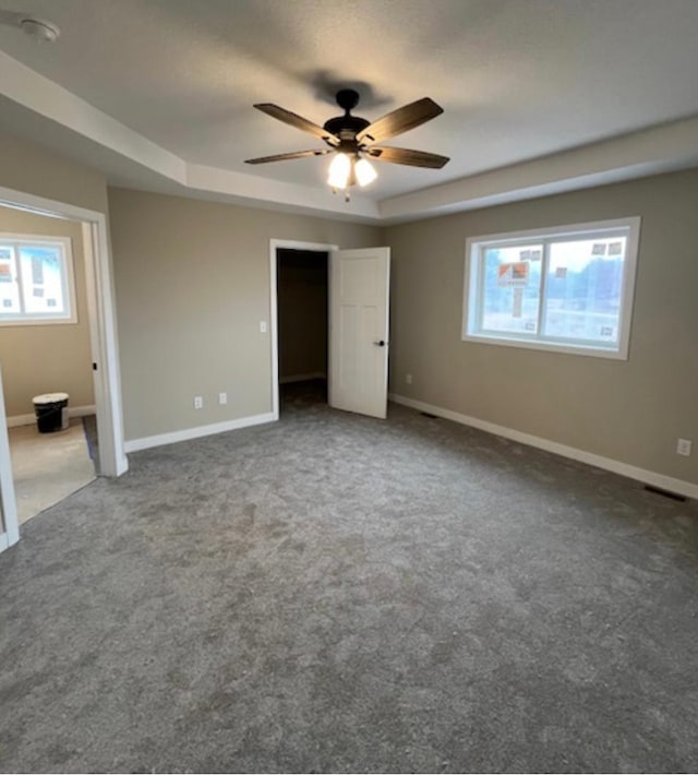 unfurnished bedroom with ceiling fan, carpet flooring, and a tray ceiling