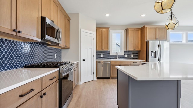 kitchen with appliances with stainless steel finishes, a center island, sink, light hardwood / wood-style flooring, and decorative light fixtures