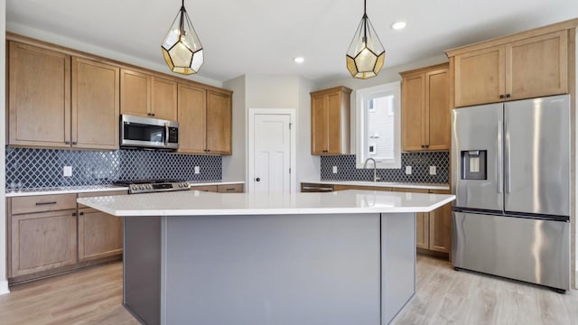 kitchen with sink, a center island, light wood-type flooring, pendant lighting, and appliances with stainless steel finishes