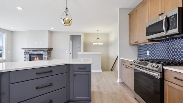 kitchen featuring decorative light fixtures, light wood-type flooring, gray cabinets, appliances with stainless steel finishes, and a stone fireplace