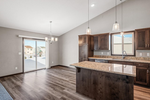 kitchen featuring light stone counters, pendant lighting, a center island, sink, and dark brown cabinetry