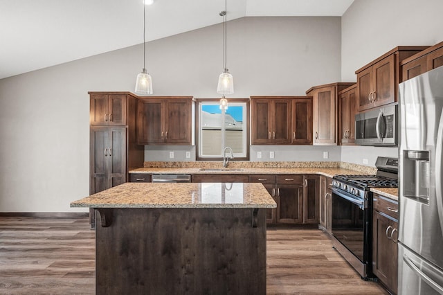 kitchen with stainless steel appliances, a kitchen island, a sink, light stone countertops, and decorative light fixtures