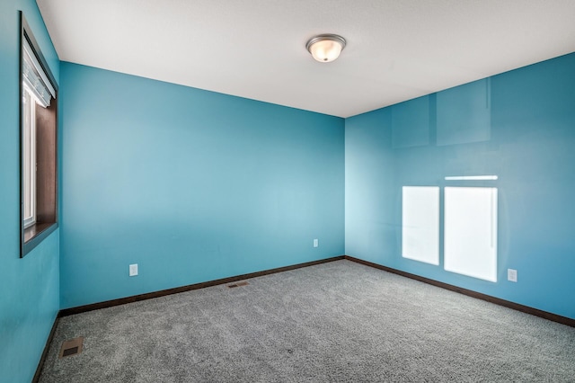 carpeted spare room featuring a healthy amount of sunlight, visible vents, and baseboards