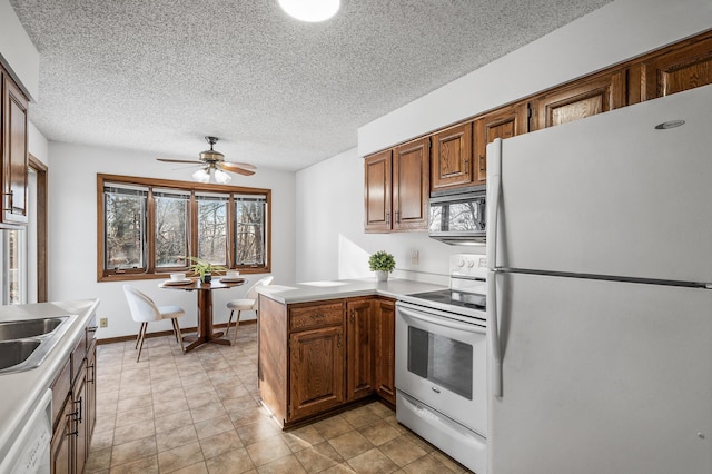 kitchen with ceiling fan, kitchen peninsula, sink, white appliances, and a textured ceiling