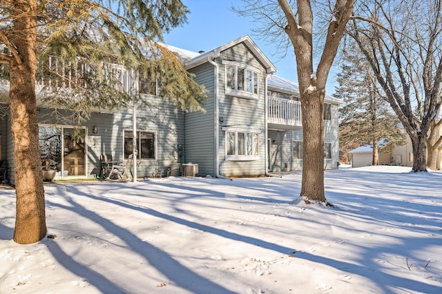 snow covered house featuring a balcony and central AC unit