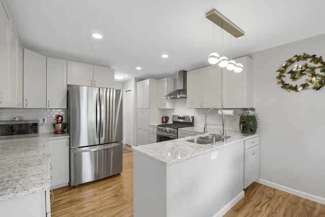 kitchen featuring white cabinetry, appliances with stainless steel finishes, pendant lighting, wall chimney exhaust hood, and sink