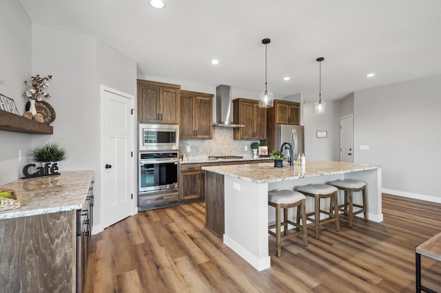 kitchen with a breakfast bar area, tasteful backsplash, decorative light fixtures, stainless steel appliances, and wall chimney range hood