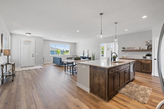 kitchen with pendant lighting, sink, a kitchen island with sink, light stone counters, and light wood-type flooring