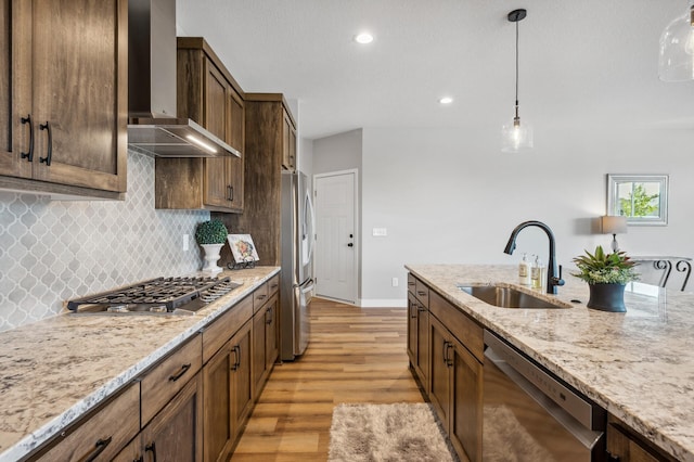 kitchen featuring sink, hanging light fixtures, appliances with stainless steel finishes, light stone countertops, and wall chimney range hood