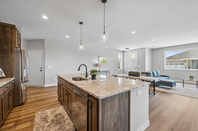 kitchen featuring appliances with stainless steel finishes, decorative light fixtures, sink, a kitchen island with sink, and light stone counters