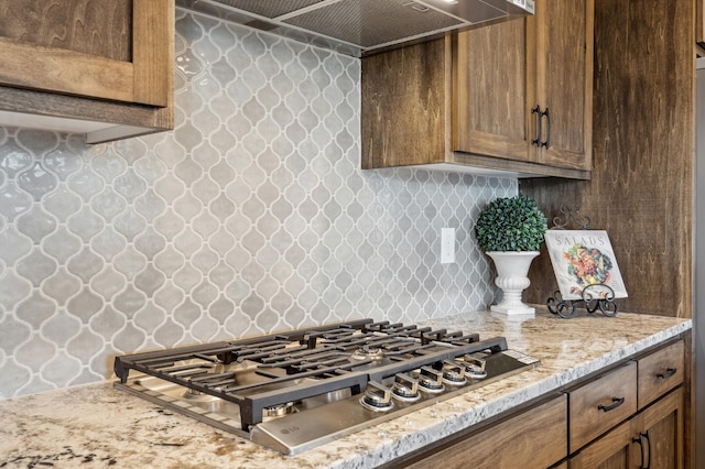 kitchen featuring wall chimney range hood, decorative backsplash, light stone countertops, and stainless steel gas stovetop