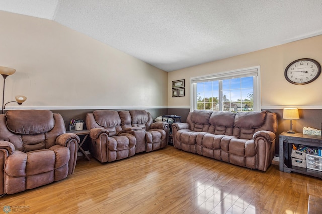 living room with a textured ceiling, vaulted ceiling, and light hardwood / wood-style floors