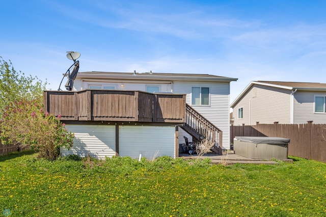 rear view of property with a hot tub, a deck, and a lawn