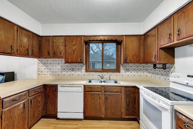 kitchen with sink, white appliances, a textured ceiling, and light hardwood / wood-style floors