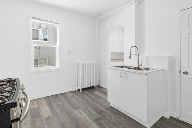 kitchen featuring gas stove, sink, hardwood / wood-style flooring, radiator, and white cabinets