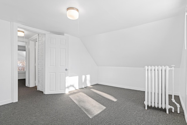 additional living space featuring radiator, vaulted ceiling, and dark carpet