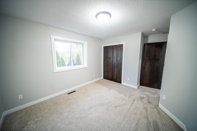 unfurnished bedroom with light colored carpet, a textured ceiling, and a closet