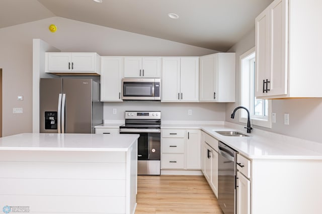 kitchen featuring stainless steel appliances, sink, white cabinetry, lofted ceiling, and a kitchen island