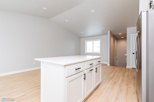 kitchen featuring vaulted ceiling, light hardwood / wood-style floors, a center island, stainless steel fridge, and white cabinetry