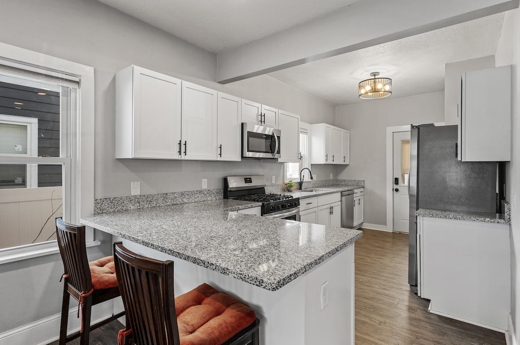 kitchen featuring a breakfast bar area, white cabinets, kitchen peninsula, stainless steel appliances, and light stone countertops