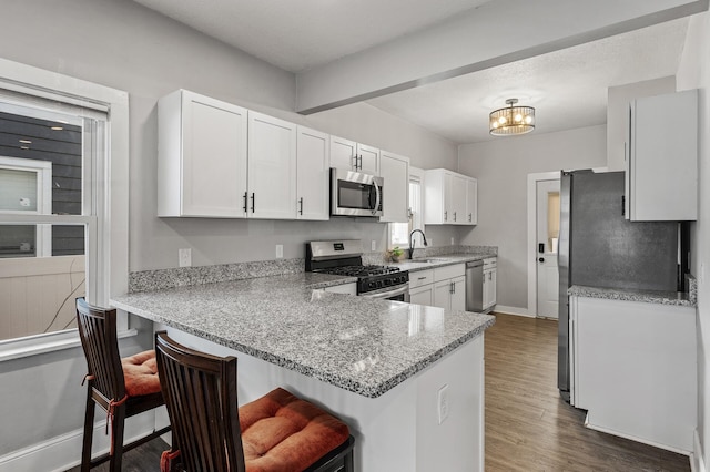 kitchen featuring a breakfast bar area, white cabinets, kitchen peninsula, stainless steel appliances, and light stone countertops