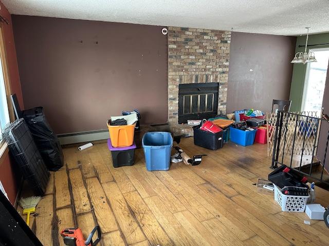 living room with a brick fireplace, baseboard heating, hardwood / wood-style floors, and a textured ceiling