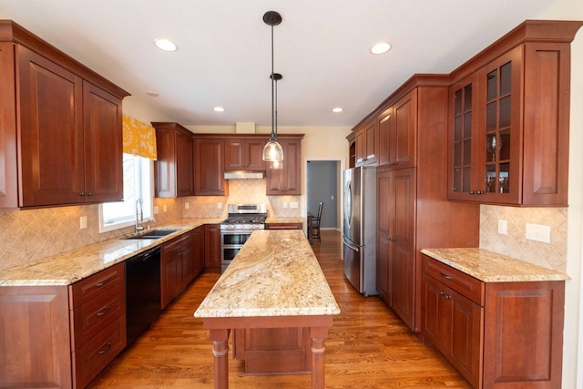 kitchen featuring stainless steel appliances, light wood-type flooring, a kitchen island, pendant lighting, and sink