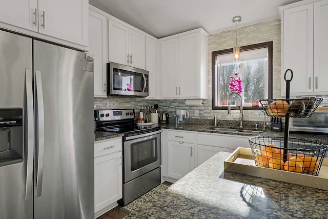 kitchen with appliances with stainless steel finishes, dark stone countertops, white cabinets, and sink