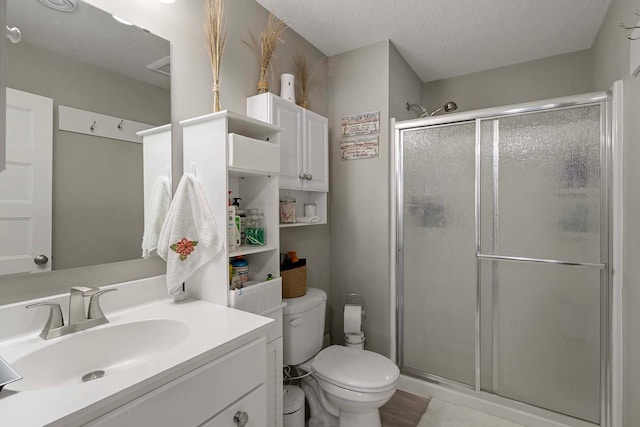 bathroom with a textured ceiling, toilet, a shower with shower door, and vanity