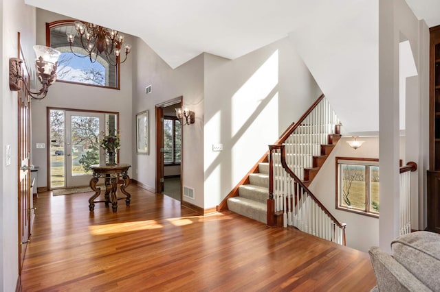 entryway featuring wood finished floors, stairway, an inviting chandelier, baseboards, and a towering ceiling