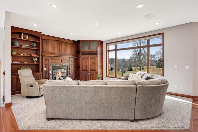 living area featuring a glass covered fireplace, recessed lighting, baseboards, and wood finished floors