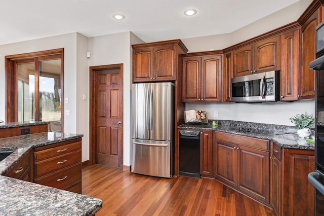 kitchen featuring dark stone countertops, stainless steel appliances, dark wood-type flooring, and recessed lighting