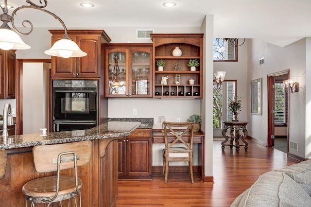 kitchen with visible vents, dark stone counters, dobule oven black, and wood finished floors