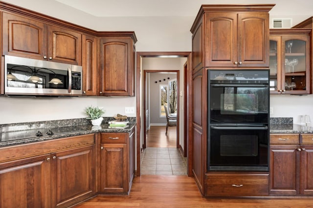 kitchen featuring visible vents, glass insert cabinets, dark stone countertops, tile patterned floors, and black appliances