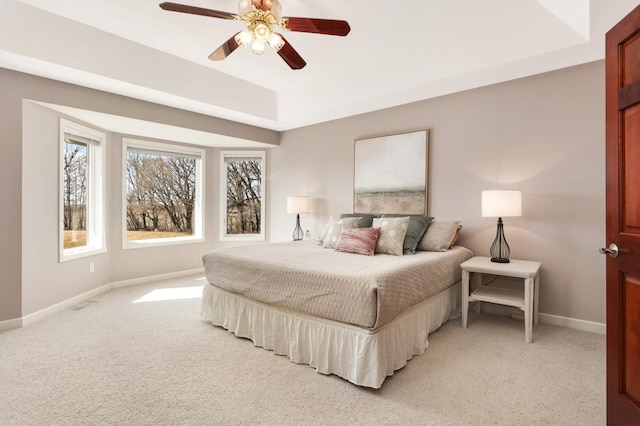 bedroom featuring baseboards, a raised ceiling, light colored carpet, and a ceiling fan