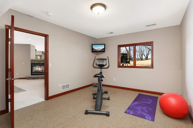 exercise room with visible vents, carpet flooring, a stone fireplace, and baseboards