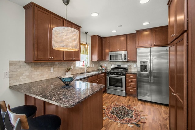 kitchen featuring kitchen peninsula, pendant lighting, stainless steel appliances, light hardwood / wood-style floors, and sink